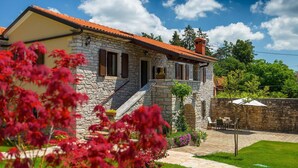 Une maison en pierre avec un toit recouvert de tuiles rouges, un petit escalier menant à l’entrée et un patio aménagé avec du mobilier d’extérieur.