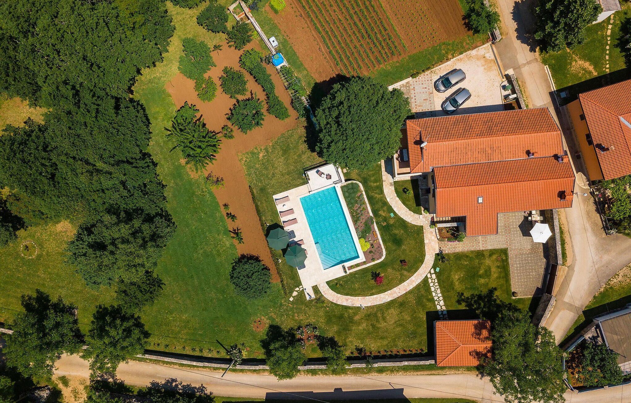 Eine Vogelperspektive eines Wohngebiets mit einem Swimmingpool, einem Haus mit rotem Dach und einem gepflasterten Einfahrt.