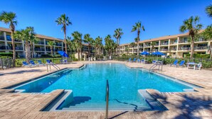 A swimming pool with lounge chairs and palm trees, surrounded by a multi-story building with balconies. - Beachfront Views from 2nd and 3rd Floor Balconies (St. Augustine Beach)