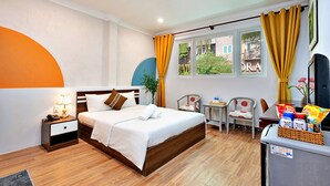 Ein Hotelzimmer mit Bett, Nachttisch, Lampe, Stuhl, kleinem Tisch und einem Fenster mit Vorhängen.