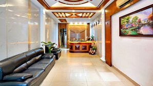 Eine Hotelhalle mit einer Rezeption, einer schwarzen Ledersofa und einem großen Gemälde an der Wand.