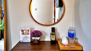 Ein Hotelrezeptionsbereich mit einem gerahmten Bild des Hotels, einer Topfpflanze, einer Fernbedienung, einer Ablage mit einer Karaffe, Gläsern und einer Wasserflasche.