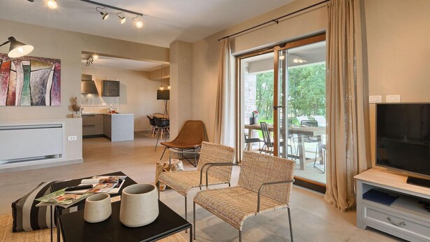 Un grand espace de vie comprenant un coin repas avec une table, des chaises en osier, un téléviseur et, au fond, une cuisine.