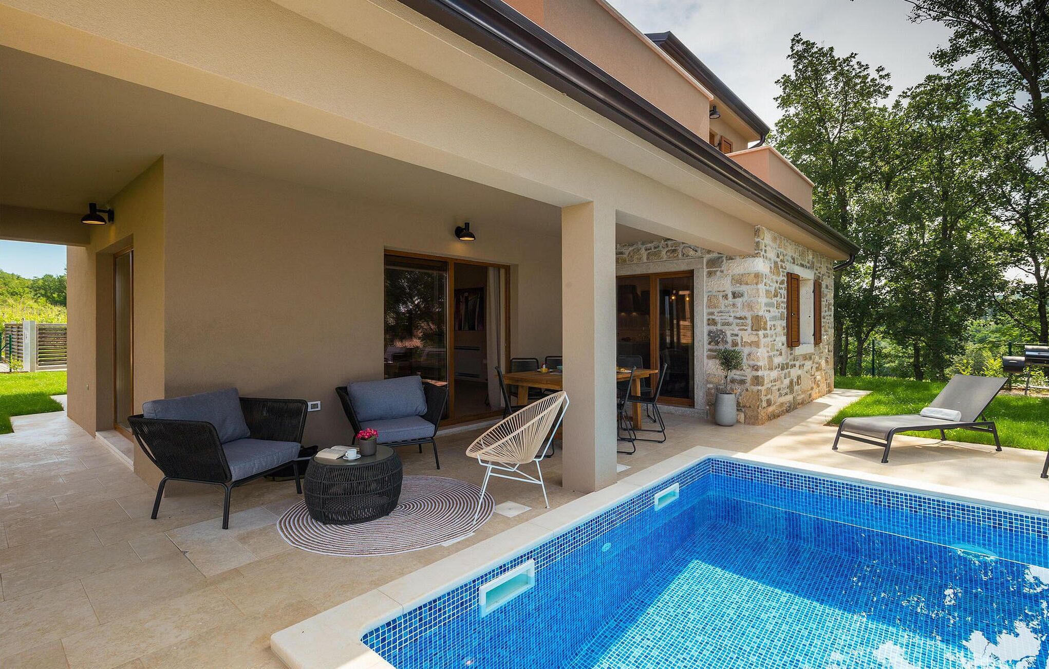 A covered outdoor area with a pool, seating, and a stone building.