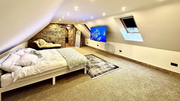 A bedroom with a sloped ceiling, a bed, a TV, and a small window. - The Stables at Historic Grade ll Listed Farm (Broadstairs)