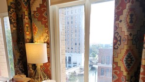 A dining area with a table set for two, a lamp, and a view of buildings through a window. - Overlooks Riverwalk/King/Downtown (San Antonio)