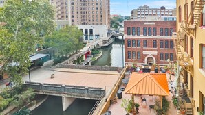 A riverside patio with outdoor seating, a bridge, and historic buildings in the background. - Overlooks Riverwalk/King/Downtown (San Antonio)