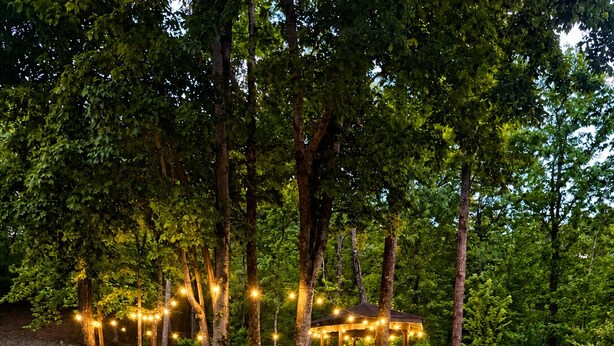 Un sentier mène à un belvédère illuminé de guirlandes lumineuses, entouré de jardins aménagés et d’arbres.