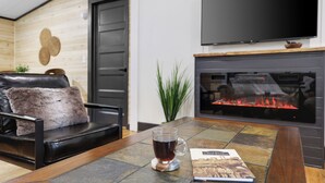 Un salon moderne avec un canapé en cuir, une tasse en verre posée sur un sous-verre, une cheminée et un téléviseur à écran plat fixé au-dessus.