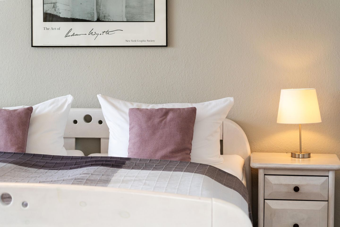 A neatly made bed with a patterned bedspread, two pillows, a bedside lamp, and a framed artwork on the wall.