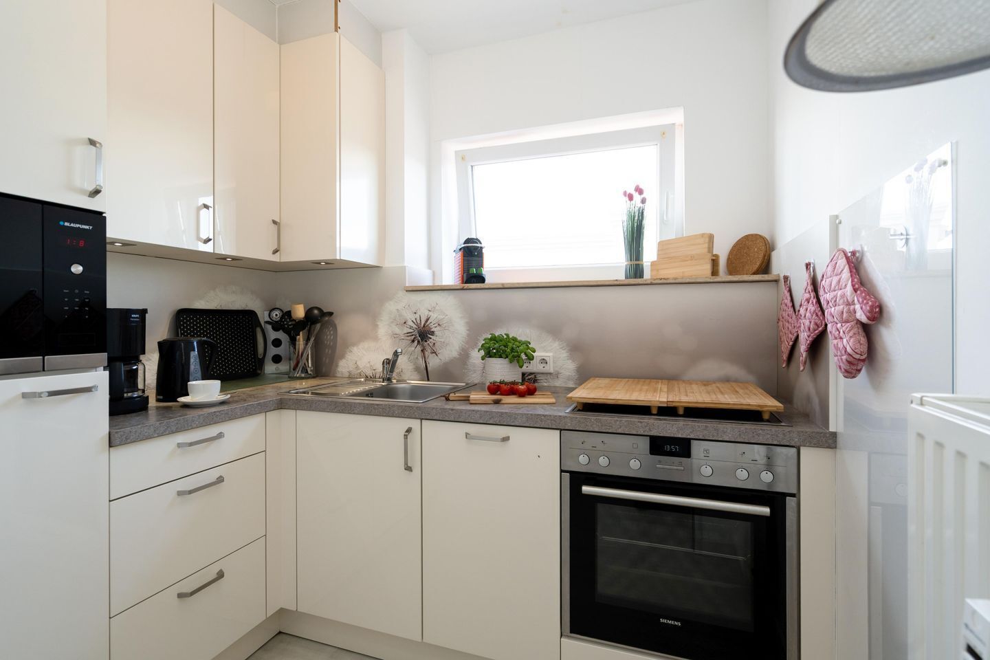 A modern kitchen with white cabinets, a black coffee maker, a Siemens oven, and a window with a view of the outside.