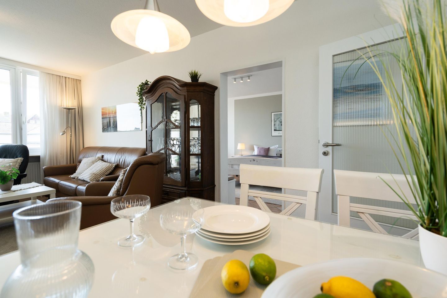 Ein modernes Wohnzimmer mit einer braunen Ledersofa, einem Glastisch und einem Essbereich mit weißem Tisch und Tellern.