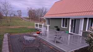 Ein überdachter Patio-Bereich mit Gartenmöbeln, einem Gewächshaus und Blick auf die umliegende Landschaft.