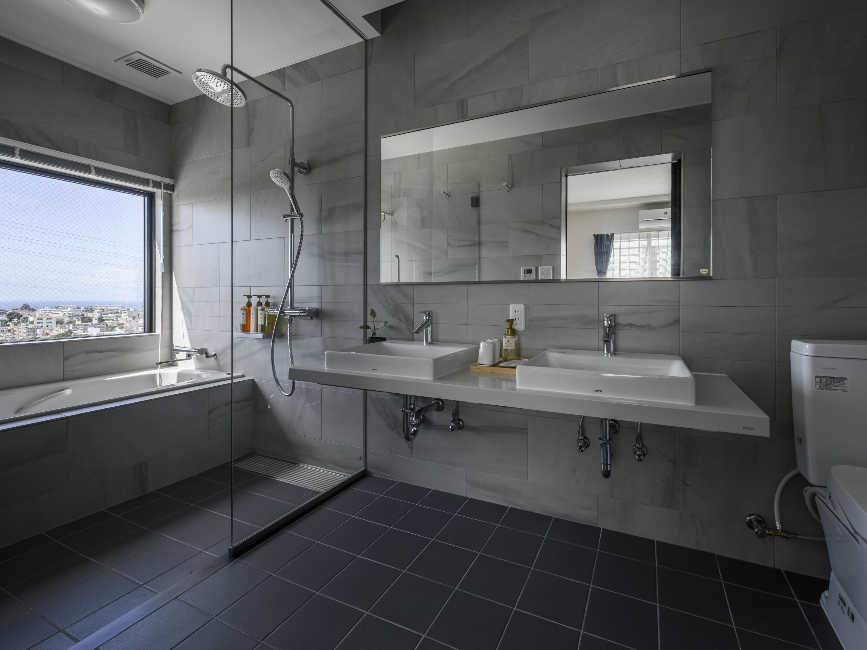 A modern bathroom with two sinks, a glass shower enclosure, and a toilet.