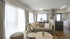 A modern living room with a sofa, ottoman, and two round tables. - &Monde. Okinawa Arena Condominium (Okinawa)