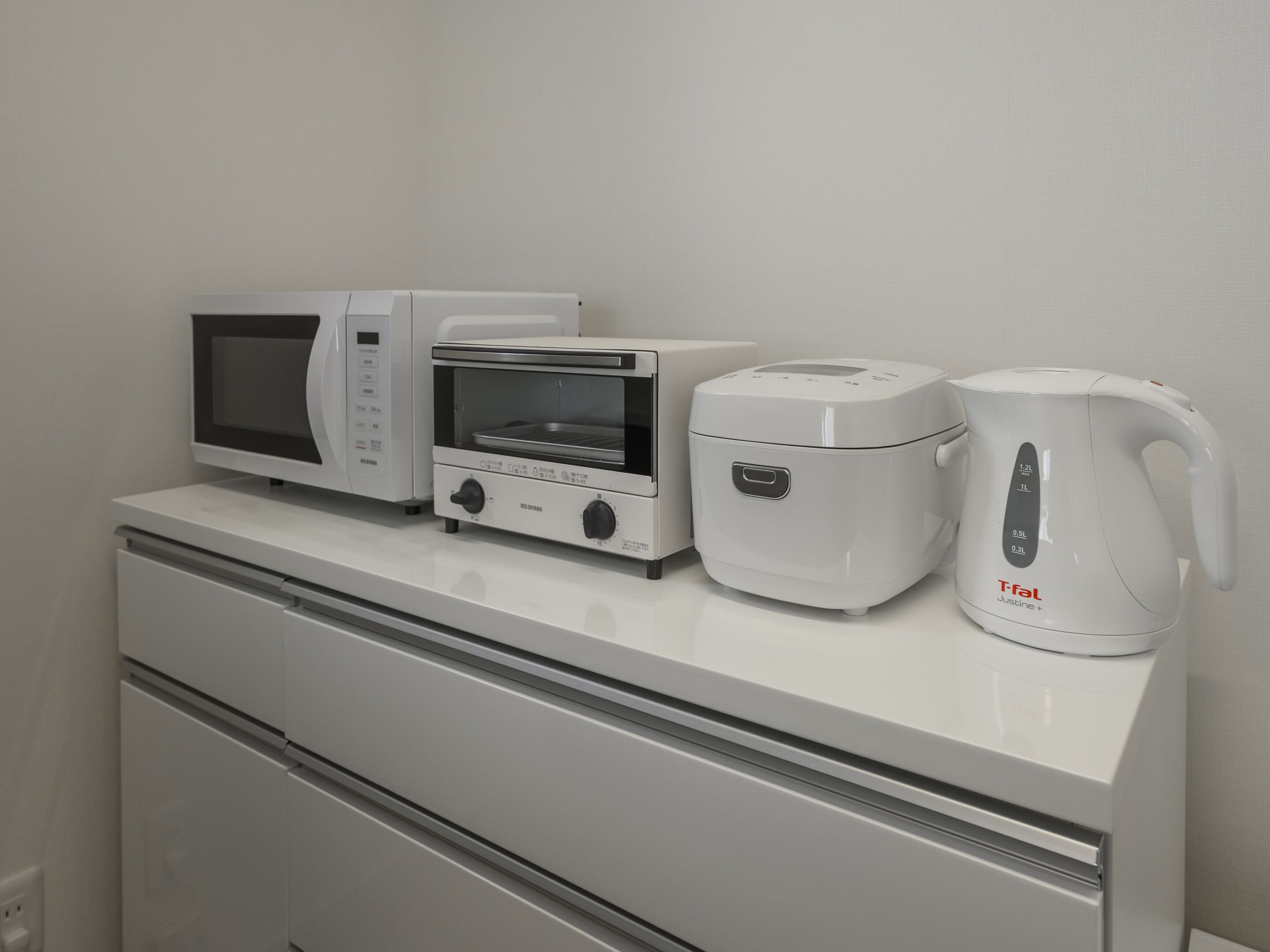 A kitchenette with a microwave, toaster, rice cooker, and coffee maker on a white countertop.
