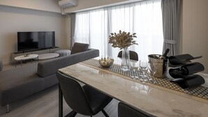 A modern living room with a flat-screen TV, grey sofa, and a dining area with a marble table and black chairs. - &Monde. Okinawa Arena Condominium (Okinawa)