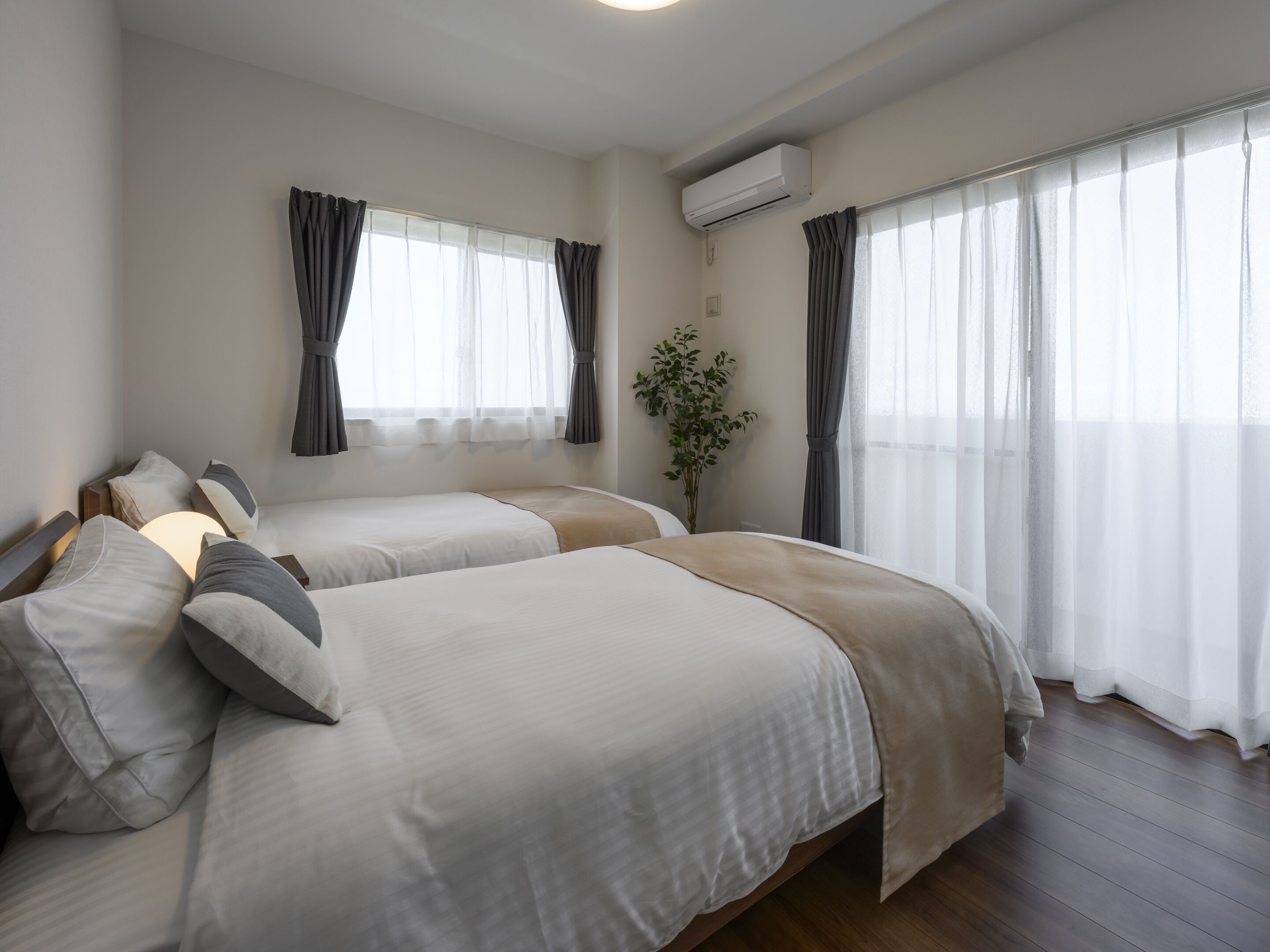 Une chambre d’hôtel avec deux lits, une plante en pot et de grandes fenêtres avec des rideaux.