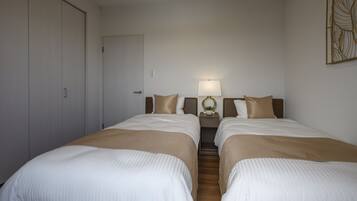 A hotel room with two beds, a wardrobe, a nightstand with a lamp, and a decorative wall piece.