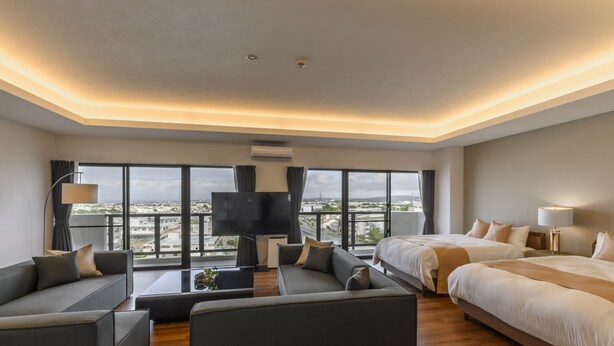 A modern hotel room with a large bed, a sofa, a TV, and a view of the city. - &Monde. Okinawa Arena Condominium (Okinawa)
