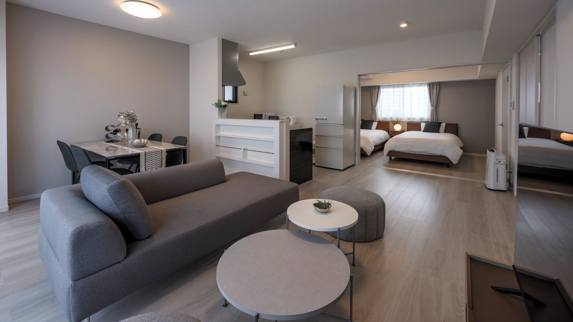 A modern hotel room with a sofa, a dining table, a small round table, a bed, a wardrobe, and a bathroom.