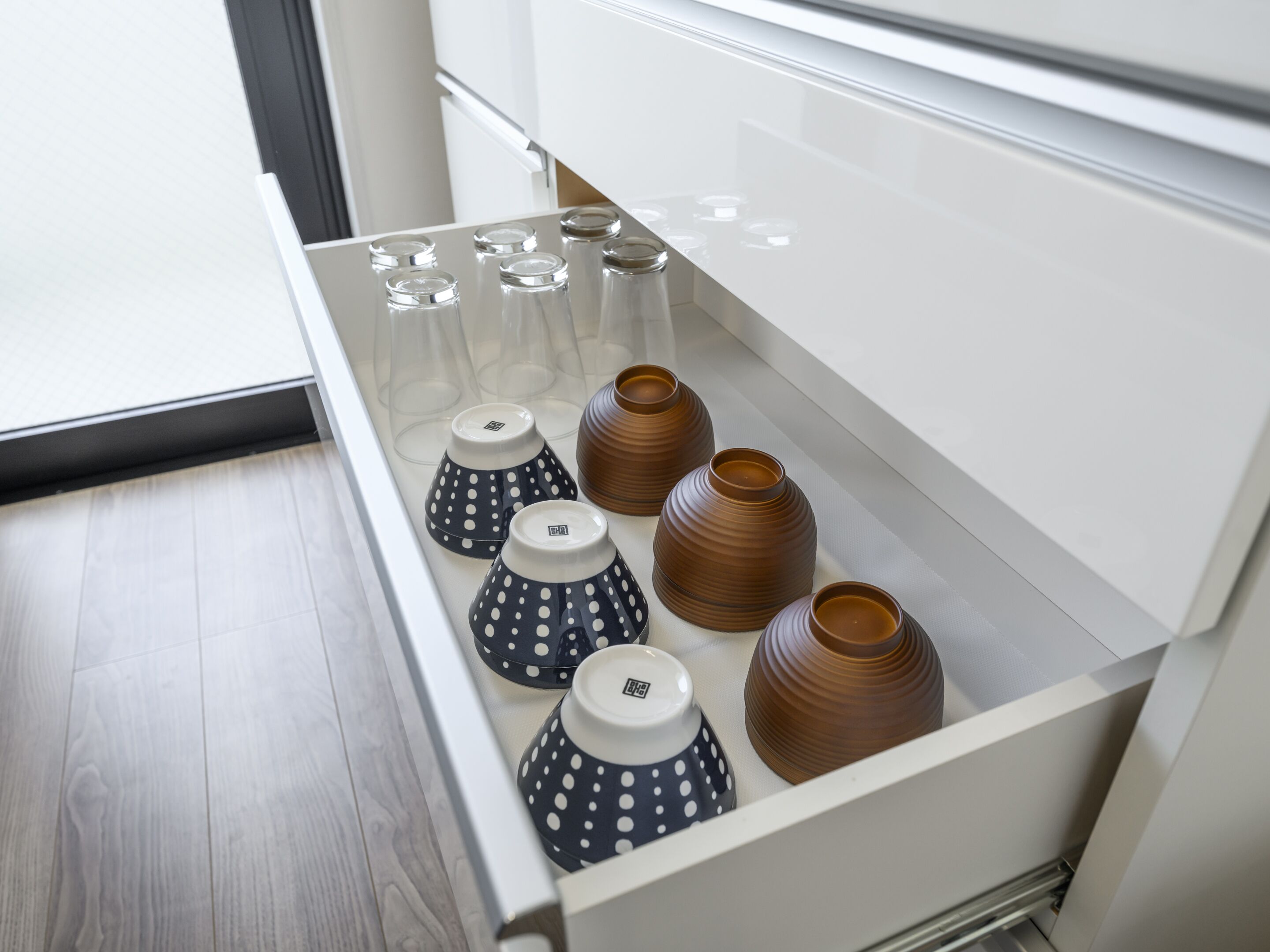 A kitchen drawer with various kitchenware including clear glass cups, black and white polka dot cups, and brown ceramic vases.