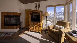 A cozy living room with a fireplace, a wooden entertainment center, a comfortable sofa, and a large window offering a mountain view. - Eolus 626 - Managed by Purgatory Resort (Durango)