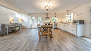 A spacious kitchen with wooden flooring, white cabinetry, and a dining area with a table and chairs. - Belacasa Where Modern Comfort Meets the Quiet of the Woods (Douglas)