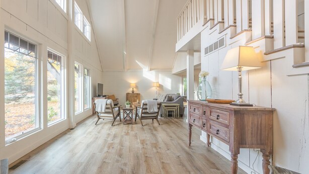 A spacious room with large windows, a wooden floor, a staircase, and a dining area with a table and chairs. - Belacasa Where Modern Comfort Meets the Quiet of the Woods (Douglas)