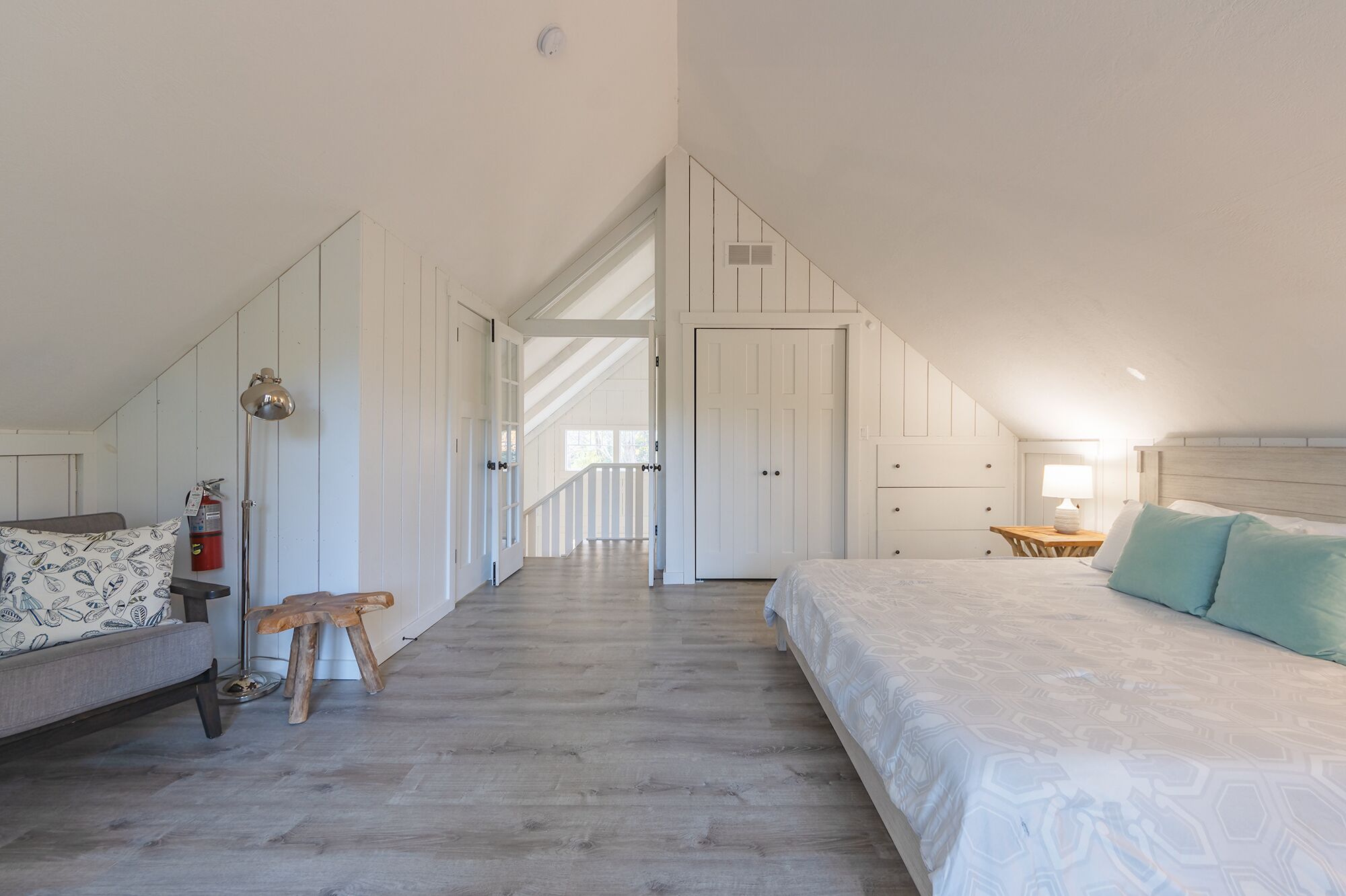 Une chambre avec un plafond en pente, un lit, une table de chevet, une lampe, une chaise et une petite table.