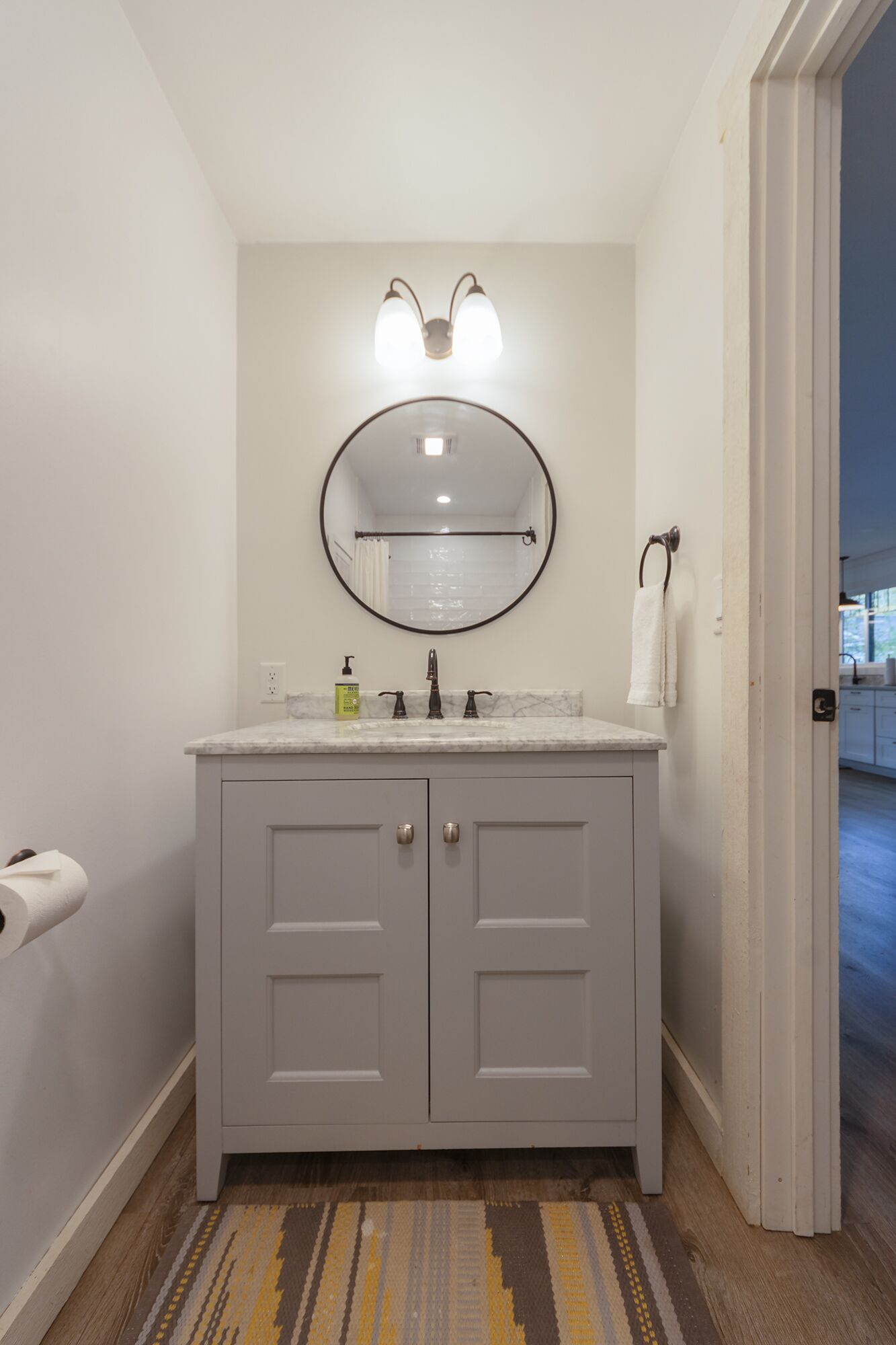 A bathroom with a marble countertop, a round mirror, and a towel rack.