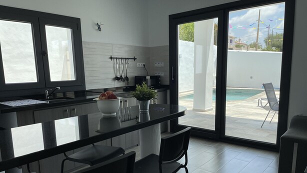 Uma cozinha moderna com ilha central, banquetas, área de refeições e vista para uma piscina ao ar livre.