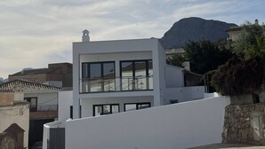 Um edifício moderno de dois andares com janelas amplas e telhado plano, cercado por um espaço pavimentado e uma parede de pedra.