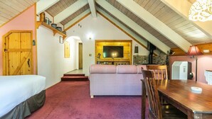 Una habitació acollidora amb un llit, un sofà amb dibuixos de quadradets, una taula de menjador i un televisor penjat a la paret.