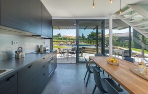 Eine moderne Küche mit einer großen Kochinsel, einem Essbereich mit Holztisch sowie Blick auf Pool und Garten.