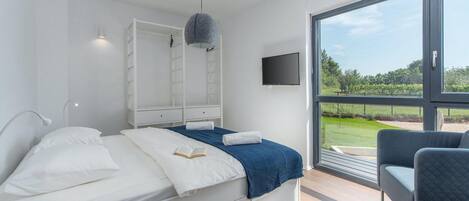 A modern bedroom with a bed, bedside tables, a TV, and a large window offering a view of the outdoors.