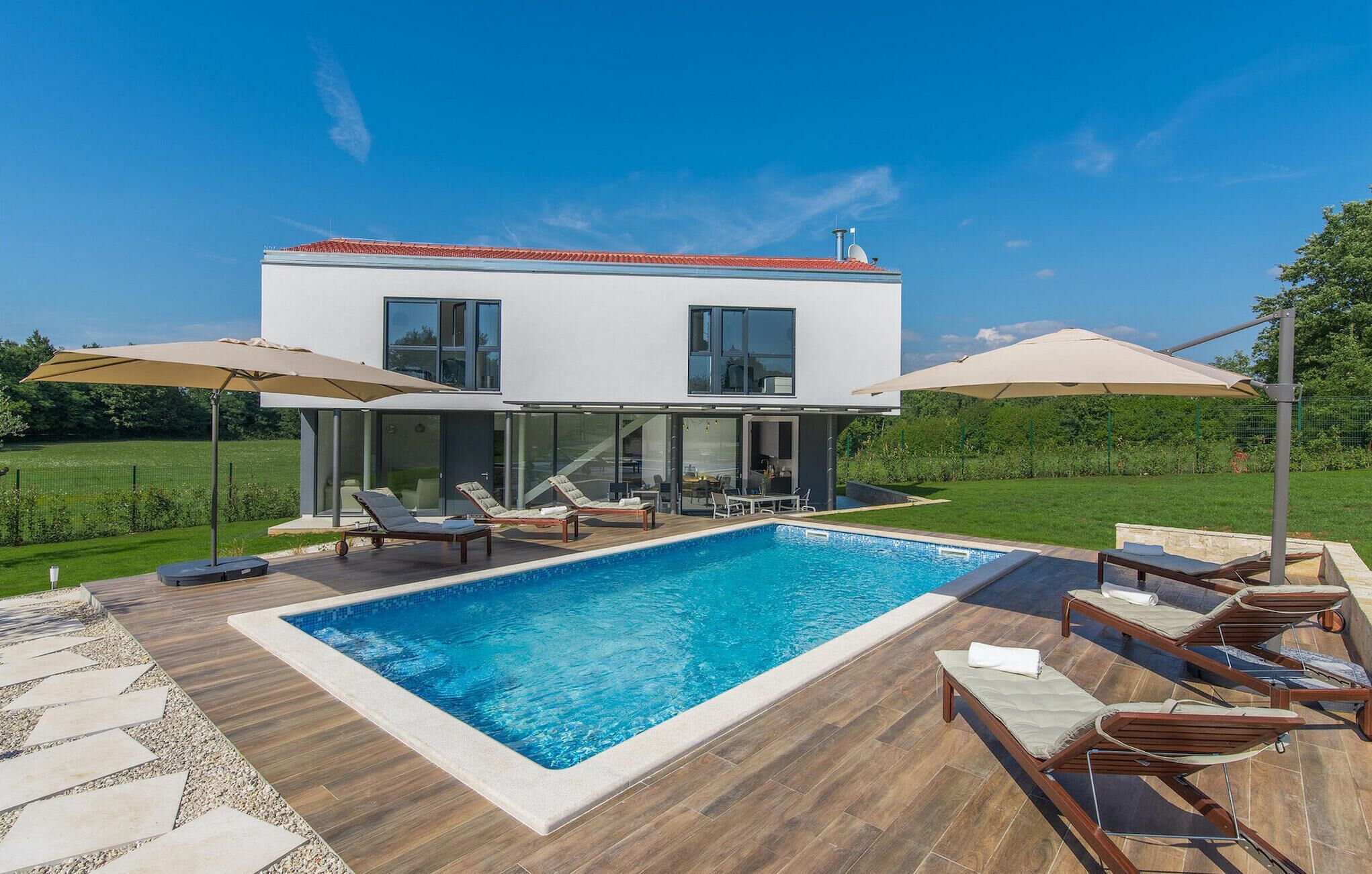 A modern two-story house with a swimming pool, outdoor seating, and a well-maintained lawn.