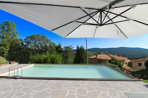A swimming pool with stone tiles, surrounded by trees and a view of hills.
