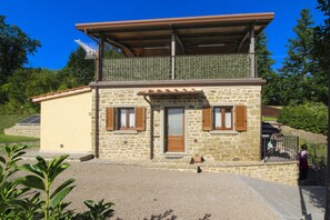 A two-story stone building with a balcony, a door, and windows with shutters.