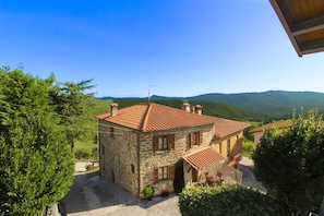 A stone house with a tiled roof, surrounded by greenery and hills.