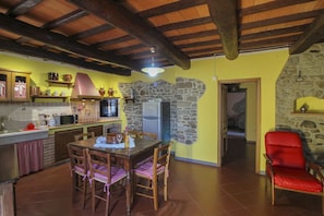 Una cocina rústica con pared de piedra, vigas de madera en el techo y un comedor con mesa y sillas.