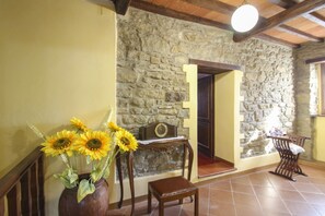 A room with a stone wall, a wooden chair, a wooden table, and a vase with sunflowers.