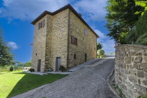 Un edificio de piedra con techo inclinado, camino de grava y una pared de piedra a la derecha.