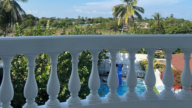 Un balcon doté d’une balustrade blanche, qui offre une vue sur une piscine et des palmiers.