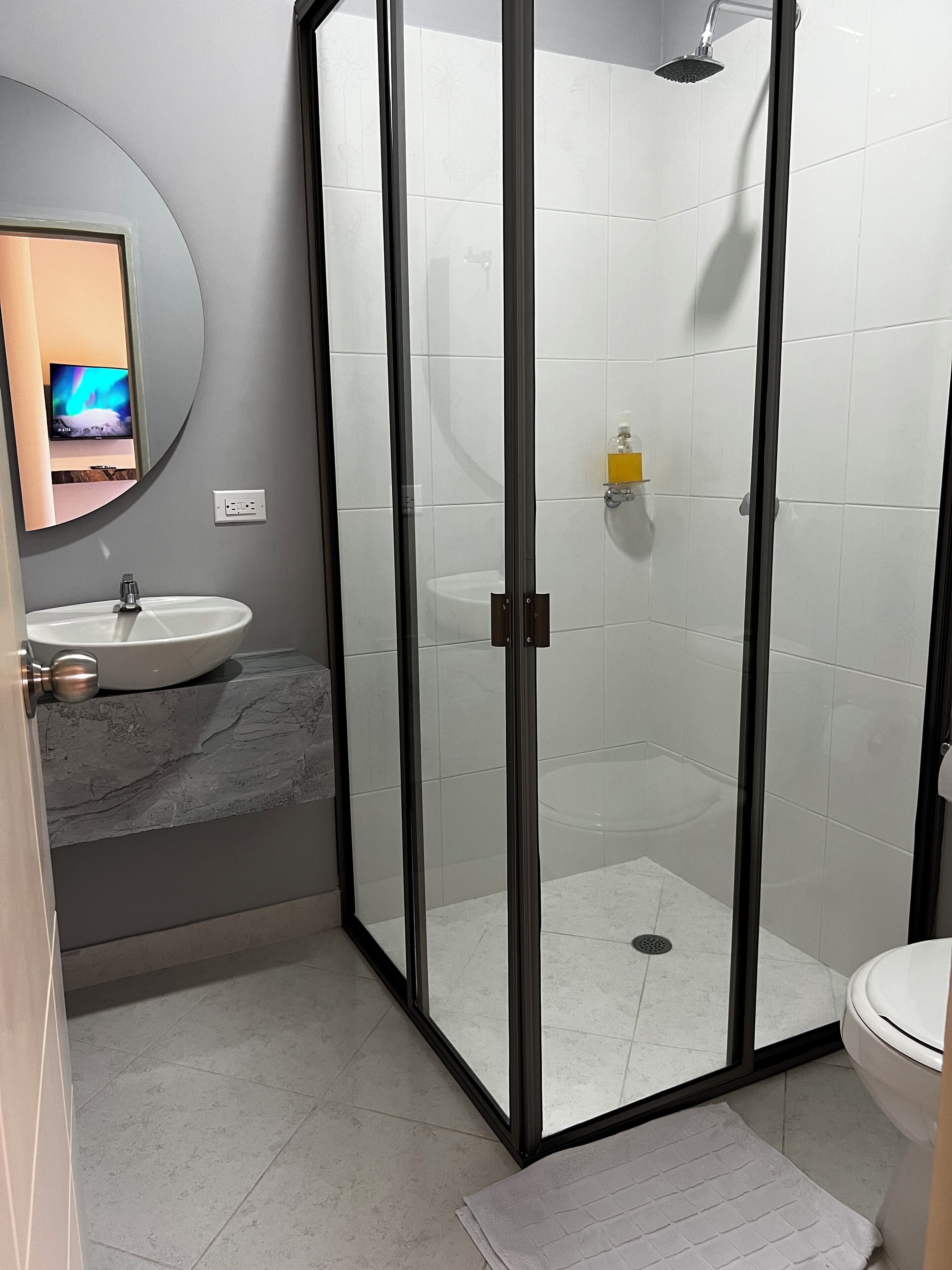Un baño moderno con cabina de ducha de vidrio, lavamanos con encimera de mármol y retrete.