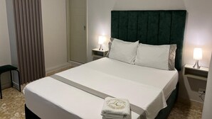 Un lit bien fait, avec des draps blancs, deux lampes de chevet et une serviette pliée posée sur le lit.