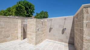 A stone-walled outdoor shower area with two showerheads and a tiled floor.