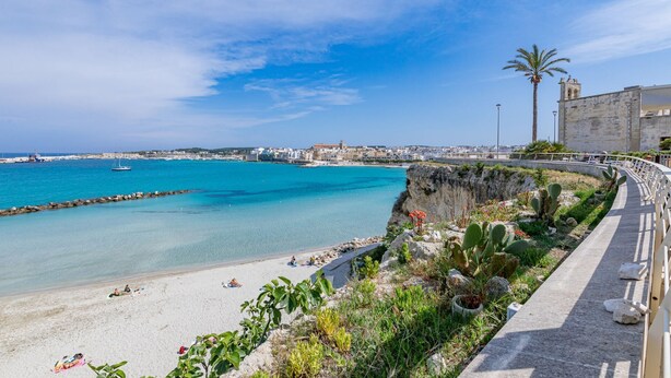 A coastal town with a beach, a historic stone building, and a clear blue sky.