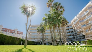 A multi-story residential building with balconies, surrounded by well-maintained grass and palm trees. - Acogedor Apartamento con Piscina a un Minuto de la Playa (Miami Platja)