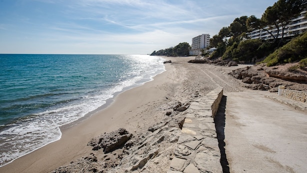 A beach with a stone pathway leading to a building with multiple balconies. - Acogedor Apartamento con Piscina a un Minuto de la Playa (Miami Platja)
